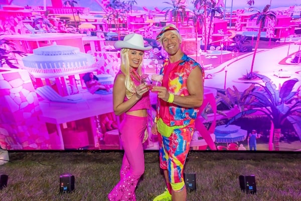 Barbie and Ken standing infront of a large pink backdrop